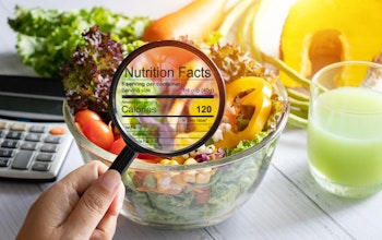 hand holding a magnifying glass illuminates nutrition and calorie information infront of a bowl of fresh crispy salad next to a calculator 