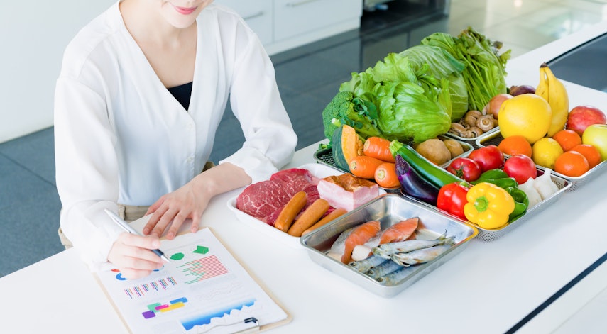 Getting food information to consumers woman in a white shirt sits at a white table filled with a range of different fruits as she overlooks food information and charts