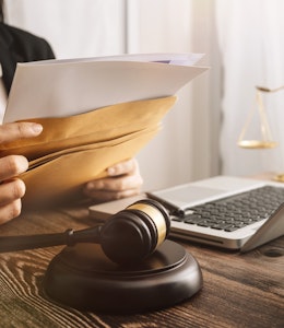 From October 2021 all food prepared and packaged on premises must display full ingredient and allergen labelling for Natasha's Law lawyer sits at a desk with laptop and dark wooden law gavel as she slips documents into a brown envelope