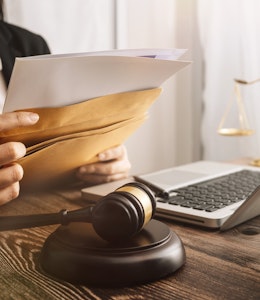 lawyer sits at a desk with laptop and dark wooden law gavel as she slips documents into a brown envelope 