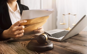 lawyer sits at a desk with laptop and dark wooden law gavel as she slips documents into a brown envelope 