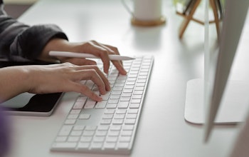 women typing on a mac wireless keyboard with an apple pen in hand and an ipad infront of the keyboard 