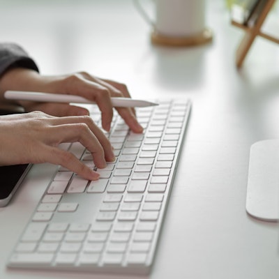 women typing on a mac wireless keyboard with an apple pen in hand and an ipad infront of the keyboard 