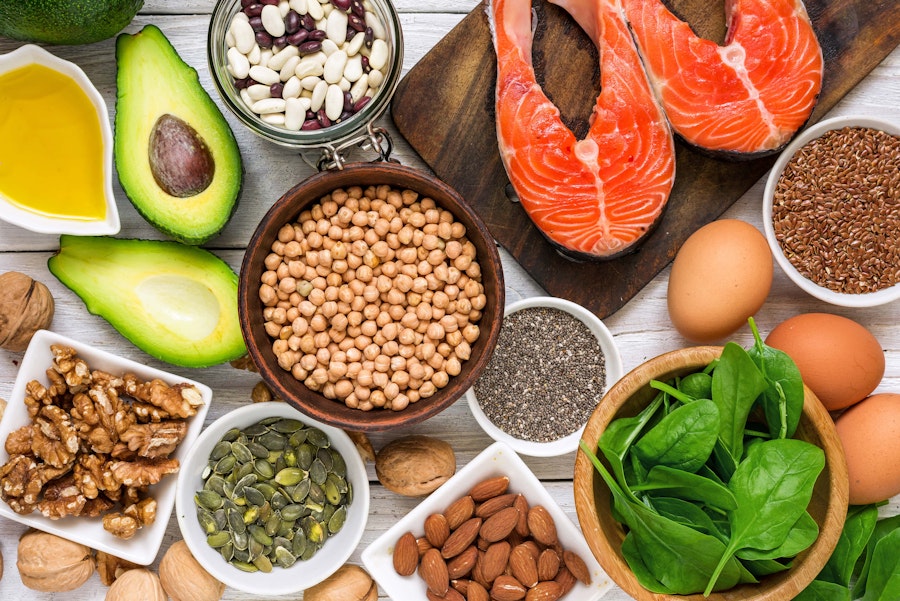 a birds eye flatlay of various nuts seeds beans and avocado spinach eggs and meat 