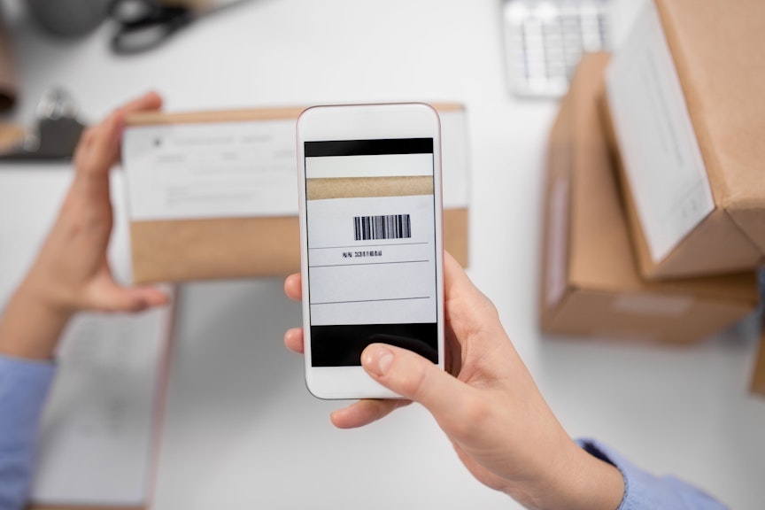 Barcodes make for easy and efficient management of your business. close up of womans hands with smartphone scanning barcode on a cardboard box