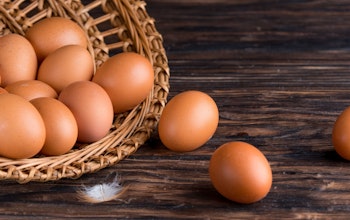 open wicker basket filled with eggs spilling out onto a dark wooden oak table and a small white feather 