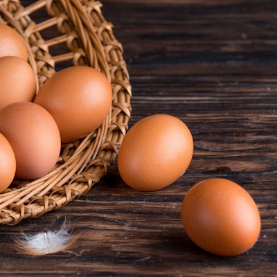 open wicker basket filled with eggs spilling out onto a dark wooden oak table and a small white feather 