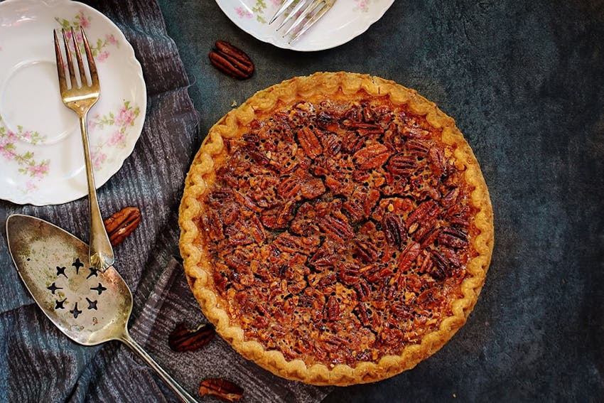 birds eye view of a golden brown nutty tart next to a vintage style saucer set with brass cutlery 