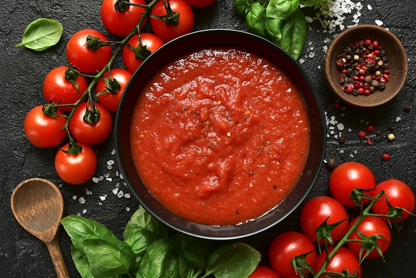 birds eye view of of a thick homeade tomato based sauce sprinkled with salt and pepper next to vines of cherry tomatoes, basil and a wooden spoon 