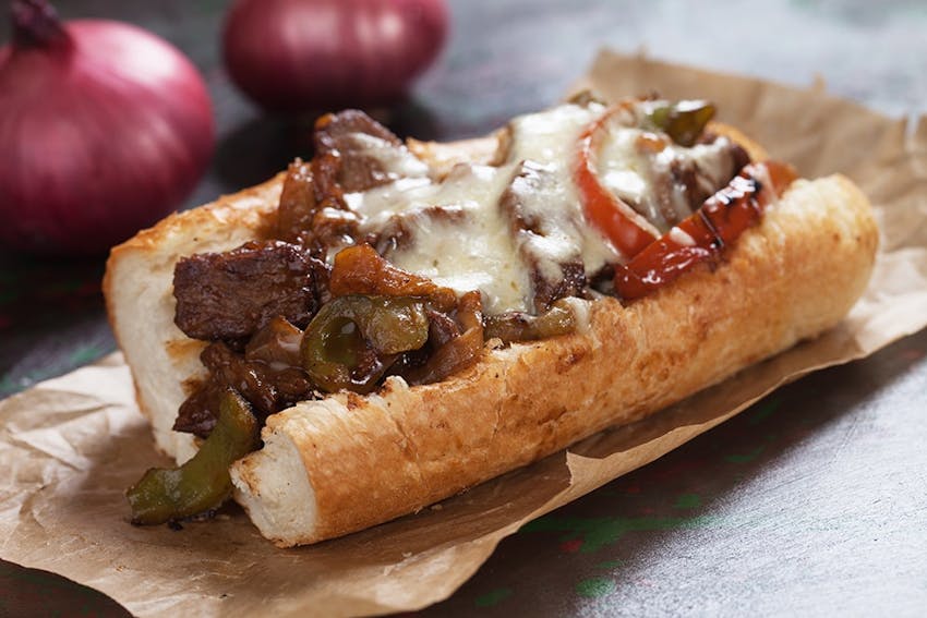 a crusty baguette with grilled chopped up steak, melted cheese, peppers and fried onions 