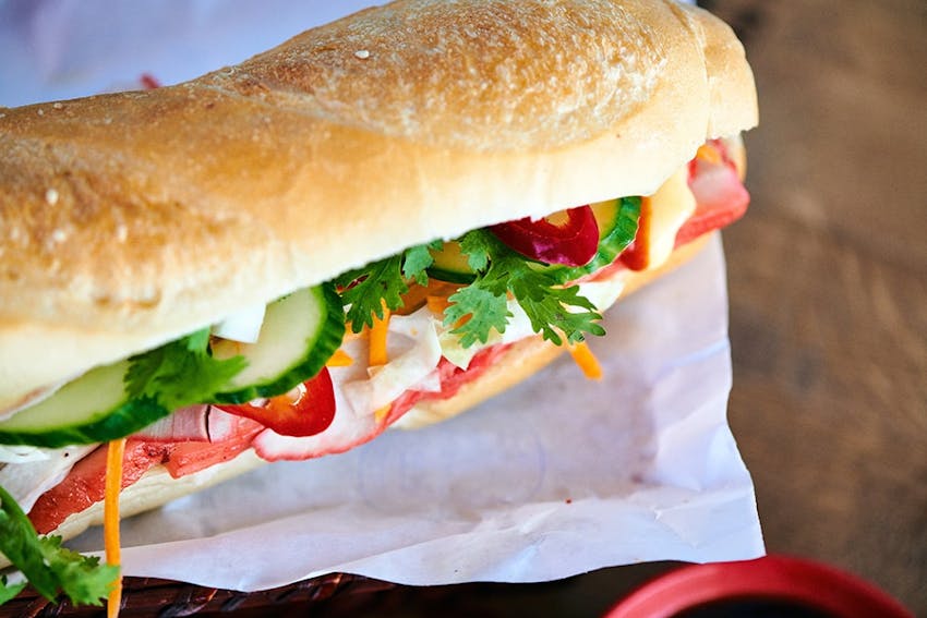 a short and crispy baguette filled with meat and vegetables on a white paper wrapper 