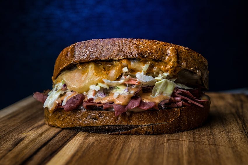 two slices of toasted crusty bread with corned beef swiss cheese sauerkraut and russian dressing on top of a wooden chopping board  