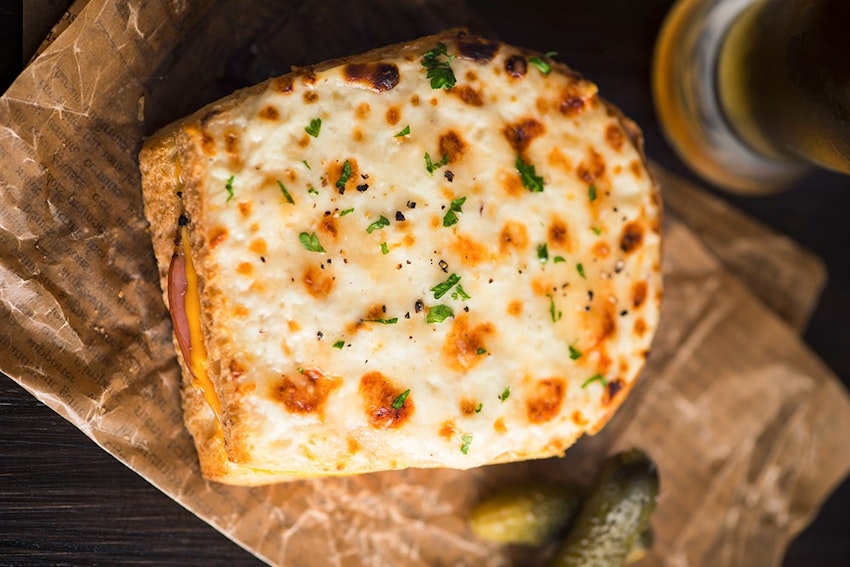 Use Pan De Mie as your bread of choice and remember to remove the crusts. toasted ham cheese and bechamel sauce sandwich on top of paper packaging and two small green gherkins