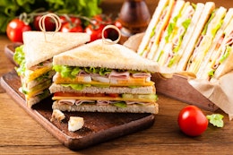 skewered double ham cheese and salad sandwich cut into small triangles on a small dark oak chopping board next to a group of vine tomatoes 
