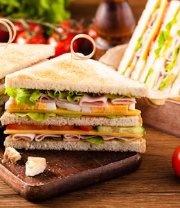 skewered double ham cheese and salad sandwich cut into small triangles on a small dark oak chopping board next to a group of vine tomatoes 