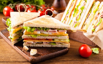 skewered double ham cheese and salad sandwich cut into small triangles on a small dark oak chopping board next to a group of vine tomatoes 