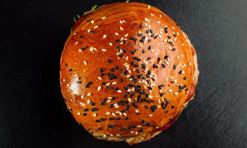 birds eye view of a golden brown brioche burger bun topped with black and white sesame seeds 