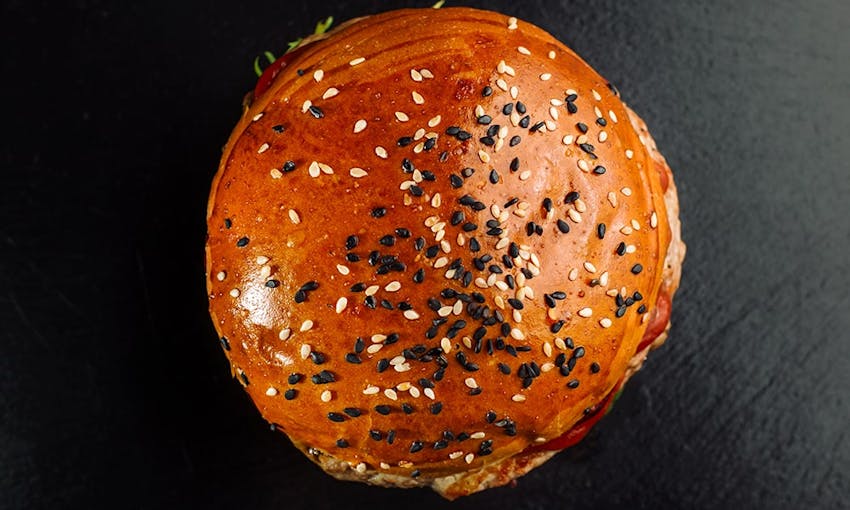 birds eye view of a golden brown brioche burger bun topped with black and white sesame seeds 