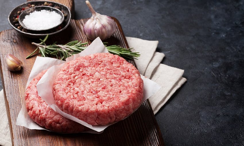 two raw circular burger patty's on top of a wooden chopping board ready to be seasoned  