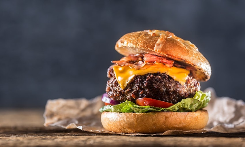 thick juicy beef burger with bacon lettuce tomato and american cheese in a bun topped with dressing 