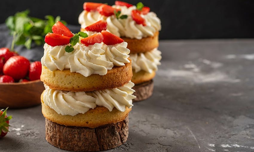 mini cakes with alternating layers of buttercream icing and sponge topped with strawberries and mini sprigs on mint  