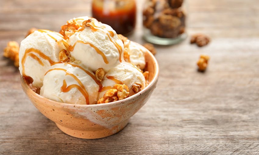 four small scoops of vanilla ice cream in a small peach coloured bowl drizzled with caramel sauce and topped with walnuts 