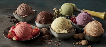 seven different colours and flavours of ice cream in stone dishes decorated with chocolate shavings and fruits 