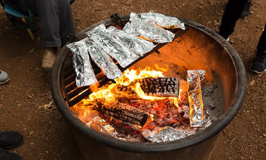 large lit bbq with foil wrapped vegetables placed on top of the grill as well as foil wrapped vegetables in the bbq pit 