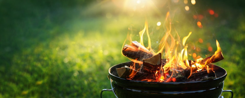 a lit freestanding barbecue with flames rising in front of a green grass back garden 