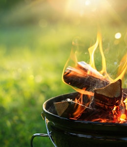 a lit freestanding barbecue with flames rising in front of a green grass back garden 