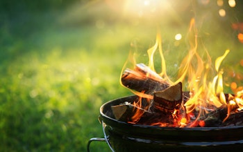 a lit freestanding barbecue with flames rising in front of a green grass back garden 