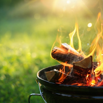a lit freestanding barbecue with flames rising in front of a green grass back garden 