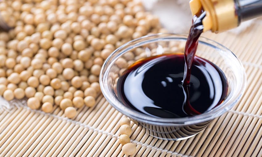 soy sauce being poured into a small saucer on top of bamboo table placer and a pile of soyabeans 