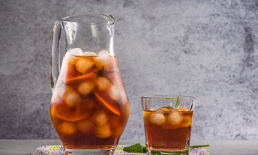 a two litre jug filled with ice cubes, fruit and peach iced tea and next to a small glass of peach iced tea with fresh sprig of mint 