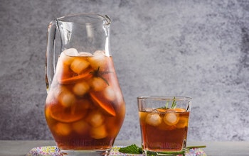 a two litre jug filled with ice cubes, fruit and peach iced tea and next to a small glass of peach iced tea with fresh sprig of mint 