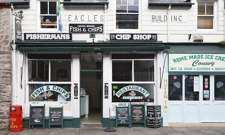 black and white traditional vintage looking storefront of a fish and chip restaurant with handwritten promotional blackboards at the front next to a home made ice cream shop 