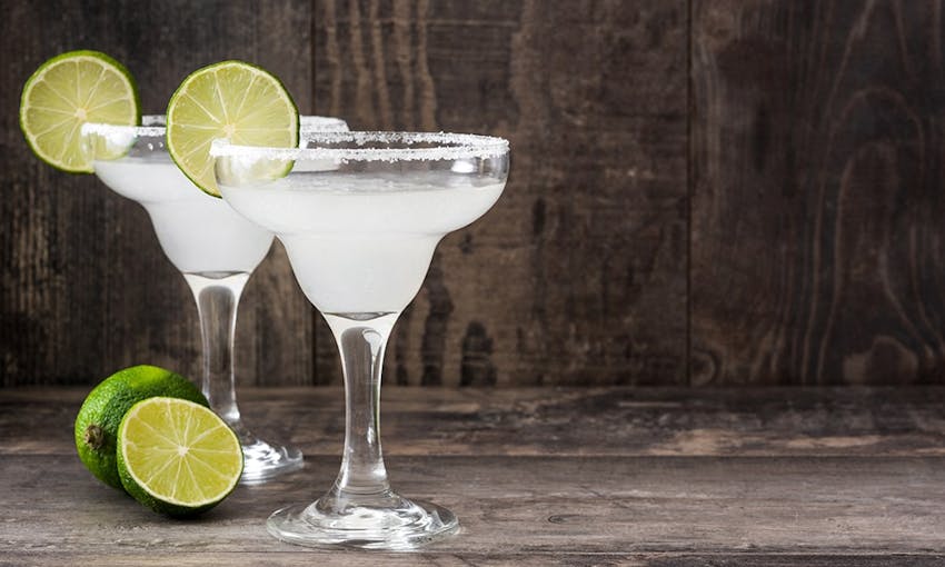 two short glasses filled with margarita with a salted rim and wedges of lime 