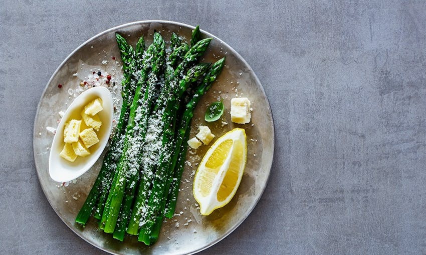 dish of asparagus sprinkled with parmesan served with cubes of butter and a wedge of lemon 