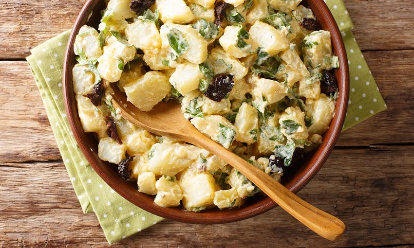 a bowl of creamy potato salad with fresh herbs and salad creamy with a wooden serving spoon 