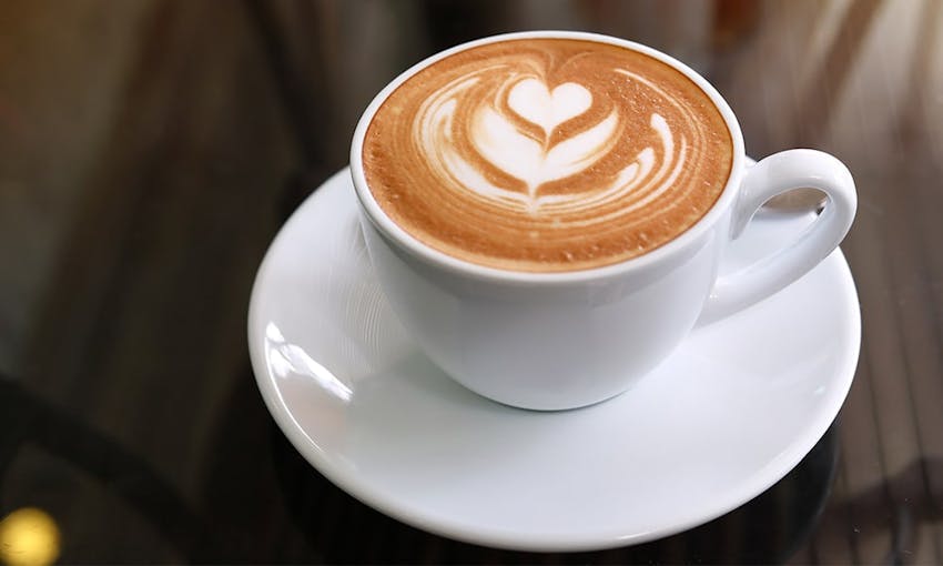 a white mug and saucer filled with a cappuccino with leaf coffee art 