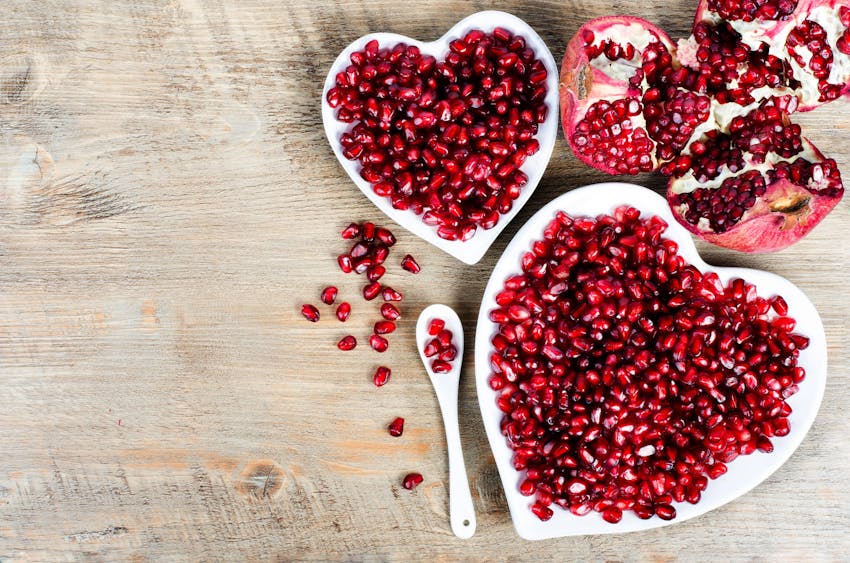 two small white heart shaped bowls filled with pomegranate seeds 