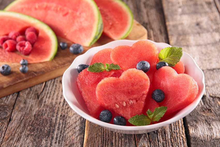 heart shaped watermelon slices in a small white bowl topped with blueberries and small mint leaves 