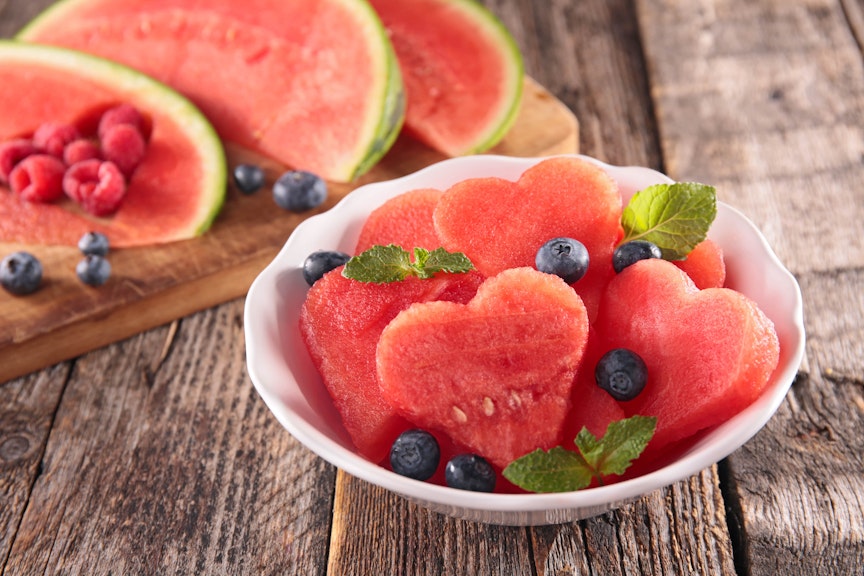 heart shaped watermelon slices in a small white bowl topped with blueberries and small mint leaves 