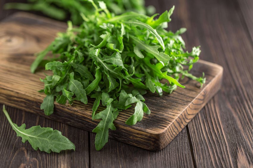 a handful or green rocket leaves on a small wooden chopping board 