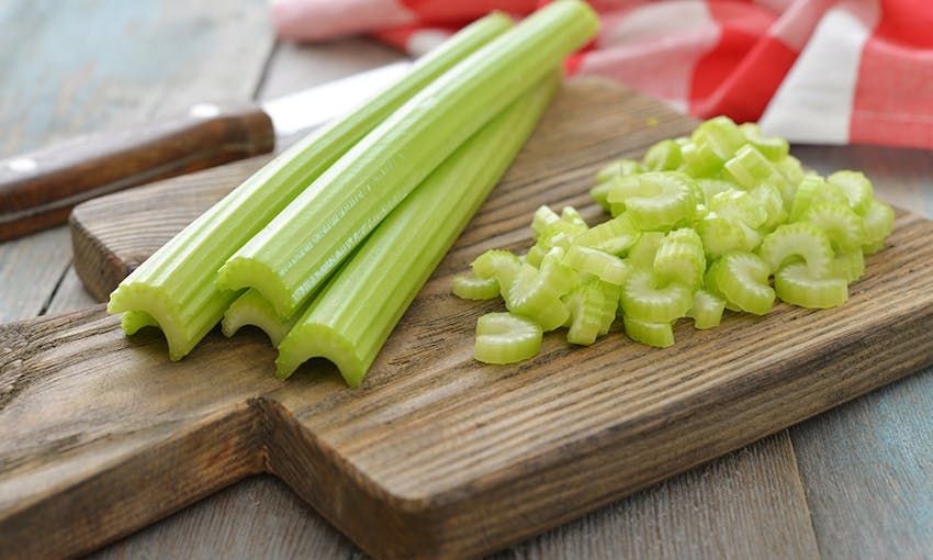 Four celery sticks next to a pile of diced celery on a wooden chopping board 