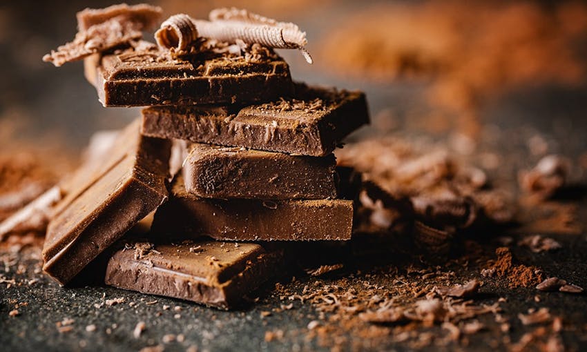 Stack of dark chocolate squares with dark chocolate shavings and dustings on a dark black surface 