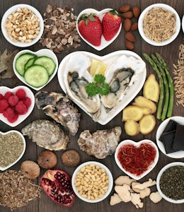 Foods to ignite your valentines day.  a birdseye view of different aphrodisiac foods, strawberries, asparagus, dark chocolate, cucumber, avocado and seeds in small circular and heart shaped dishes on a wooden table