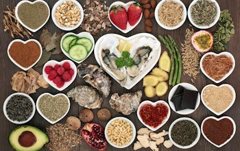 Foods to ignite your valentines day.  a birdseye view of different aphrodisiac foods, strawberries, asparagus, dark chocolate, cucumber, avocado and seeds in small circular and heart shaped dishes on a wooden table
