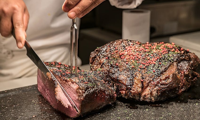 a chef slicing two large joints of roasted season beef on the kitchens surface with sharp shiny silver utensils 