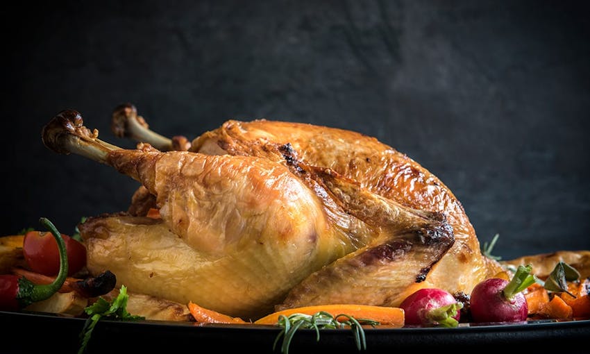 a whole roast turkey with crispy skin surrounded by roasted vegetables 